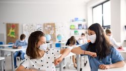 Zwei Schülerinnen mit Mundschutz reichen sich die Ellenbogen