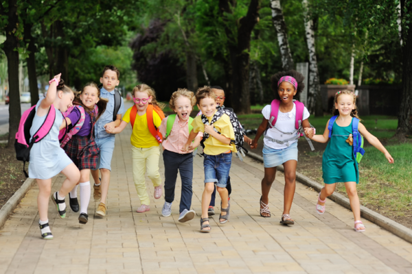 Schulkinder freudig in einer Reihe draußen zur Schule laufend