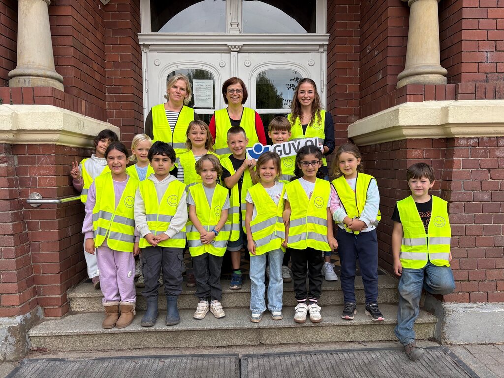 Theresa Wieting übergibt die Sicherheitswesten an Melanie Fuchs, Lehrkraft, und Erstklässlerinnen und Erstklässler der Grundschule Röwekamp