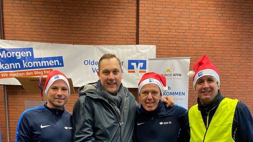Organisator Matthias Huber steht mit Mitgliedern der Laufgruppe des GUV OL vor der Bühne. Sie tragen Weihnachtsmützen.