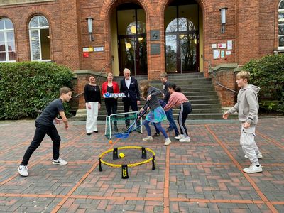 Schüler und Schülerinnen des Herbartgymnasiums zeigen ihr neues Unihockeyspiel für die aktive Pause, das vom GUV OL bezuschusst wurde. Im Hintergrund sind die Verantwortlichen der Schule und des GUV OL zu sehen 