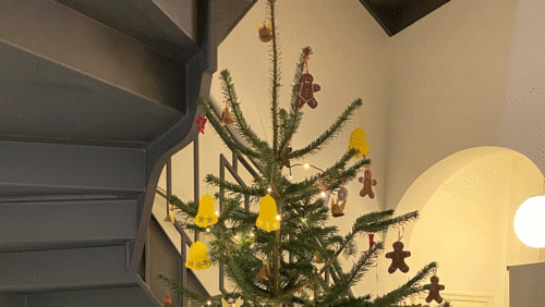 Der von den Kindern geschmückte Tannenbaum mit Anhängern aus braunem, roten und gelben Tonpapier und strahlenden Lichtern.