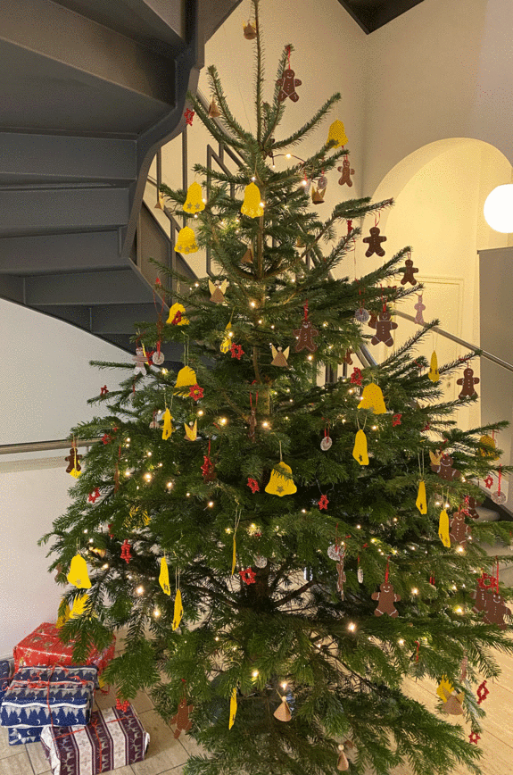 Der von den Kindern geschmückte Tannenbaum mit Anhängern aus braunem, roten und gelben Tonpapier und strahlenden Lichtern.