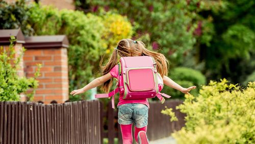 Mädchen mit Zöpfen und Schulranzen auf dem Rücken läuft einen Weg entlang