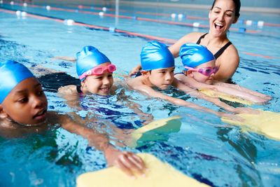 Kinder mit Badekappe beim Schwimmenlernen unterstützt von einer Schwimmkraft