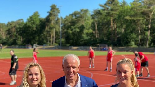 Auf dem Sportplatz in Hatten freuen sich die Koordinatorinnen des Host Town Programs Samantha Westphal, Stadt Oldenburg und Leonie Schulte, Gemeinde Hatten, über den Besuch von Michael May, Geschäftsführer des GUV OL