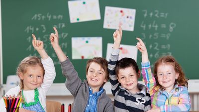 Vier Schülerinnen und Schüler vor einer Tafel melden sich