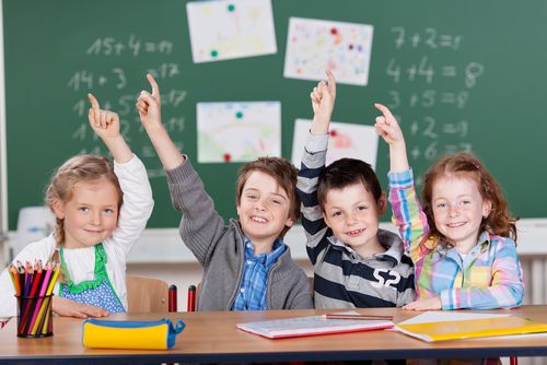 Vier Schülerinnen und Schüler vor einer Tafel melden sich 