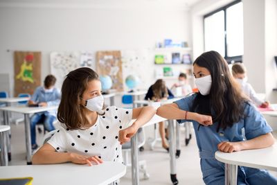 Zwei Schülerinnen mit Mundschutz reichen sich die Ellenbogen