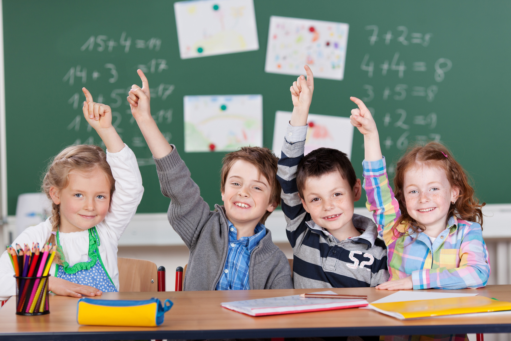 Vier Schülerinnen und Schüler vor einer Tafel melden sich